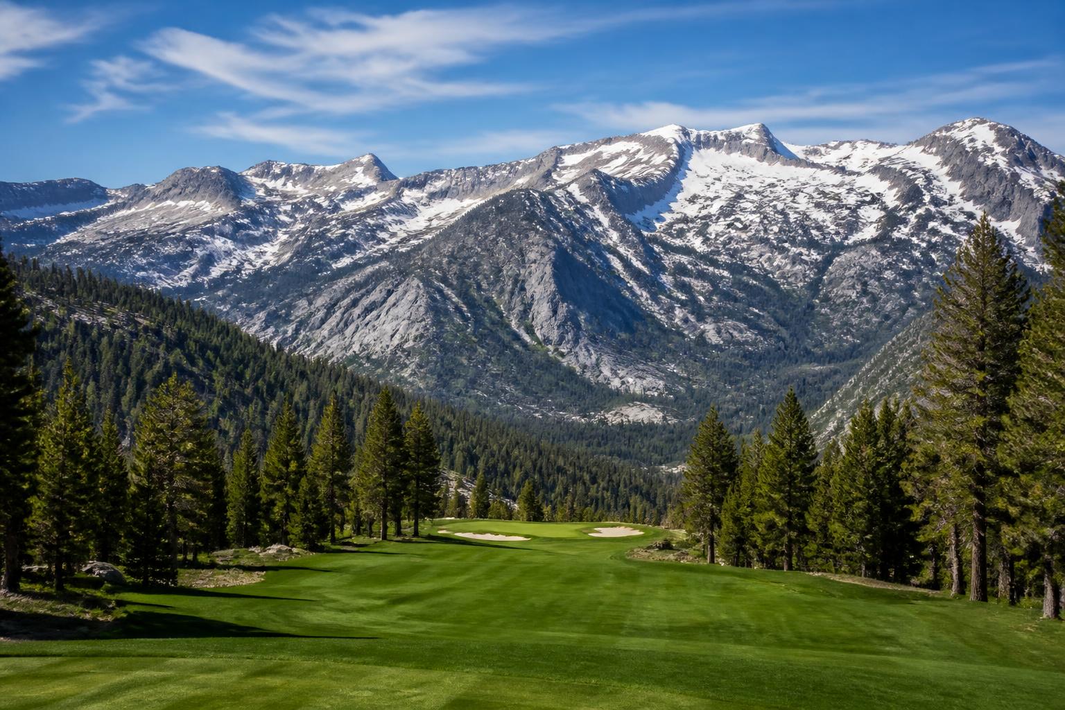Mountain golf course with snow-capped peaks and tall pine trees in the background